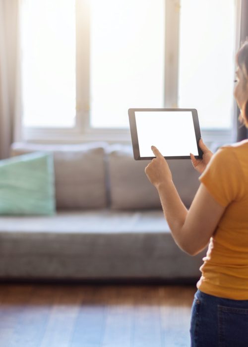 Young woman holding blank digital tablet, using smart home control system app